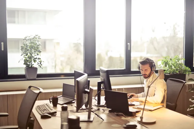 Mann mit Kopfhörern arbeitet am Computer in einem hellen Büro