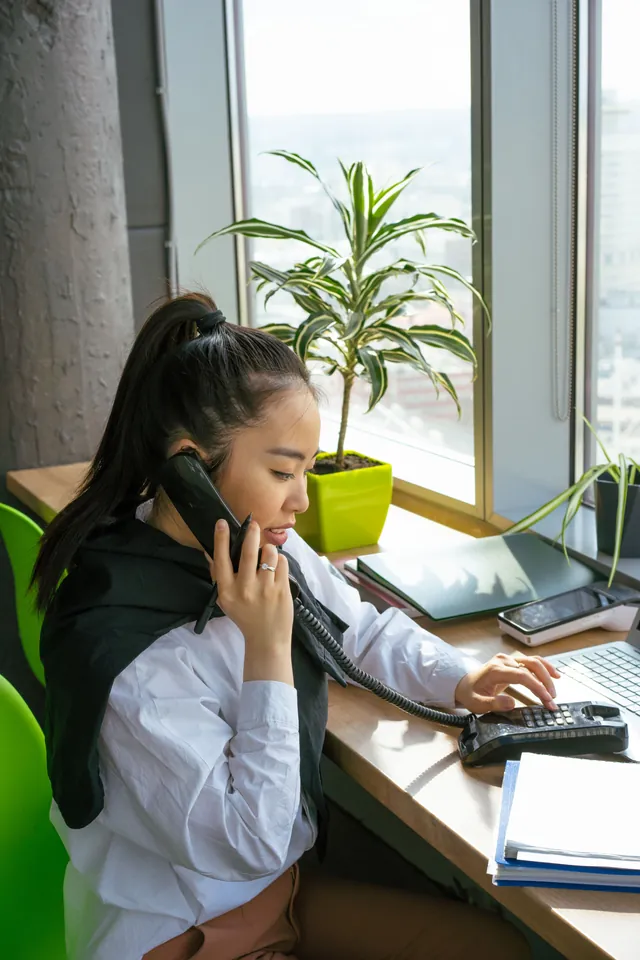 Femme à son bureau qui parle au téléphone en tapant au clavier