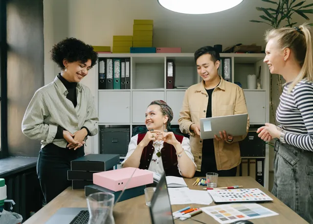 Equipo pequeño conversando en la oficina alrededor de una mesa con muestras y un portátil
