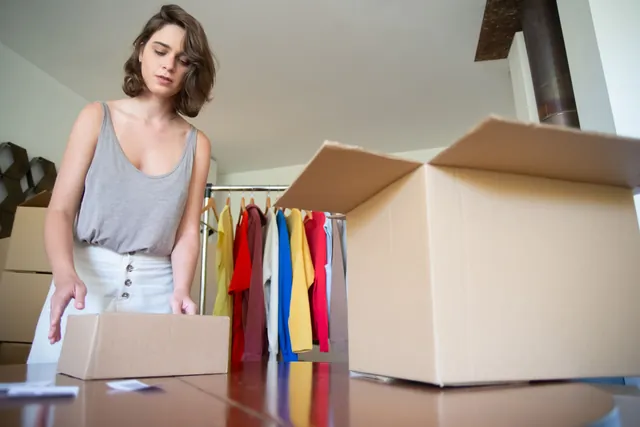 Frau packt ein Paket mit Kleidung neben einem Kleiderständer mit Produkten